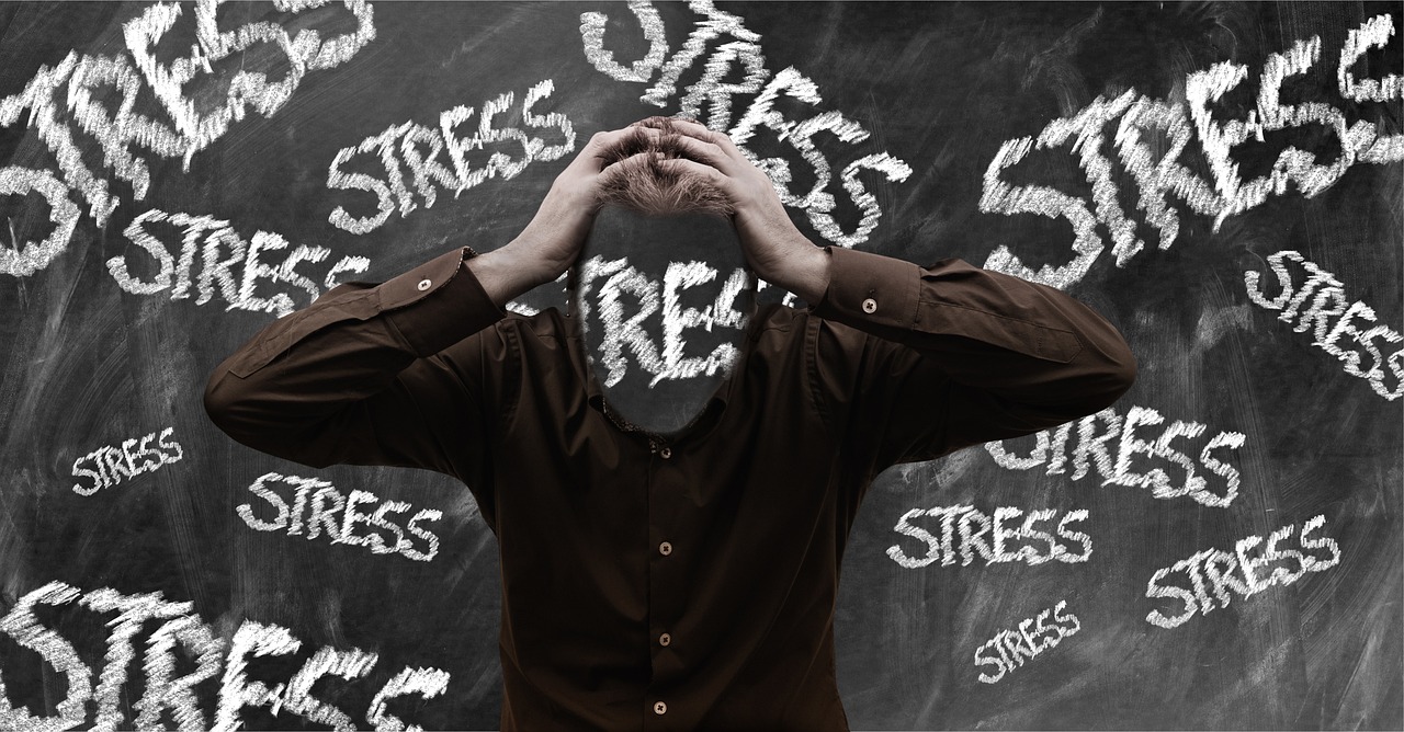 Persoon met handen op het hoofd voor een krijtbord vol met het woord stress, als illustratie van burn-out en mentale overbelasting op het werk.