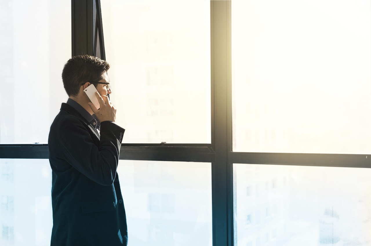 Ondernemer die telefonisch overlegt bij een kantoorraam, als illustratie van zakelijke risico’s, claims en financiële gevolgen van fouten.